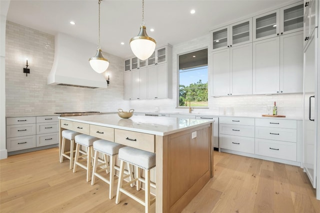 kitchen with decorative backsplash, custom range hood, a breakfast bar, a center island, and light wood-type flooring