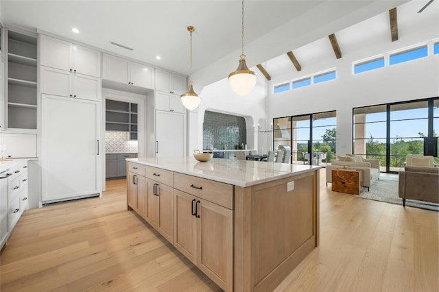 kitchen with beamed ceiling, light wood-type flooring, a kitchen island, and decorative backsplash