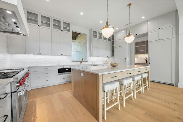 kitchen with range with two ovens, a breakfast bar, light wood-style floors, a kitchen island, and wall chimney exhaust hood