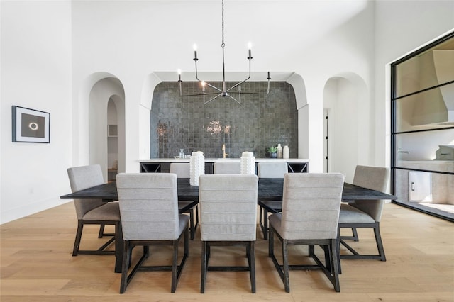 dining room with light wood-style floors, a high ceiling, arched walkways, and a notable chandelier