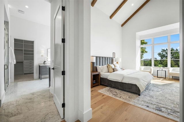 bedroom featuring light wood finished floors, visible vents, beamed ceiling, a spacious closet, and high vaulted ceiling