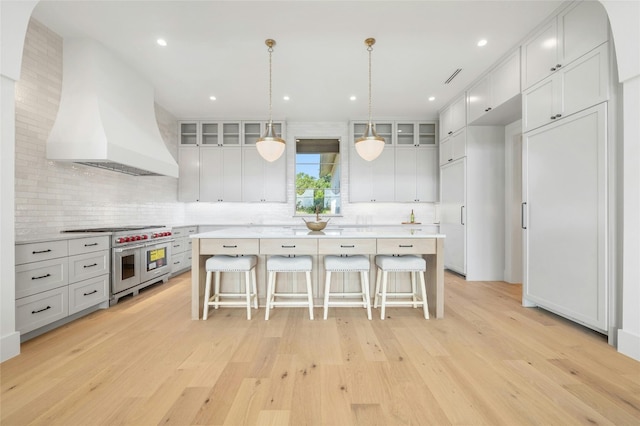 kitchen featuring decorative backsplash, double oven range, premium range hood, and light hardwood / wood-style flooring