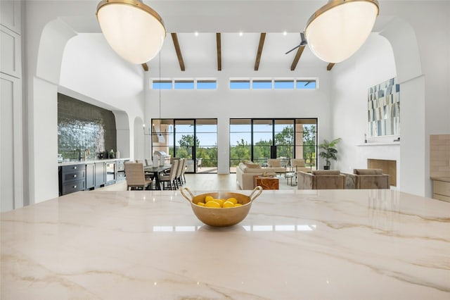 living area with ceiling fan, a high ceiling, a fireplace, and beamed ceiling