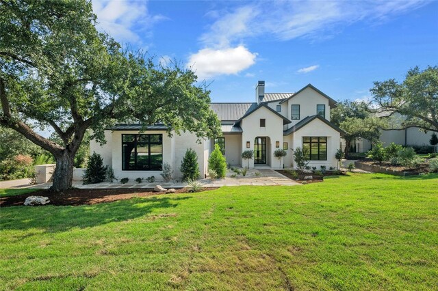 back of house featuring metal roof, a yard, stucco siding, a standing seam roof, and a chimney