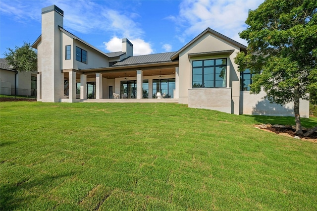 back of property with a yard, a chimney, a standing seam roof, a patio area, and metal roof