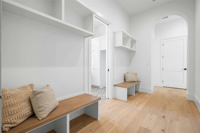 mudroom featuring arched walkways, light wood-style flooring, and baseboards