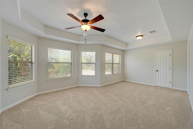 spare room with a raised ceiling, a wealth of natural light, ceiling fan, and light colored carpet