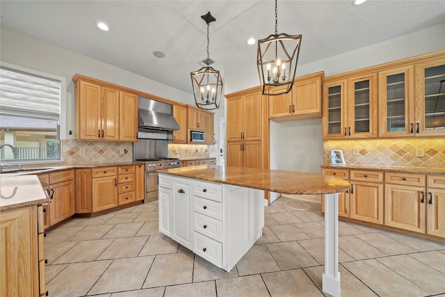 kitchen featuring appliances with stainless steel finishes, wall chimney exhaust hood, sink, decorative light fixtures, and a center island