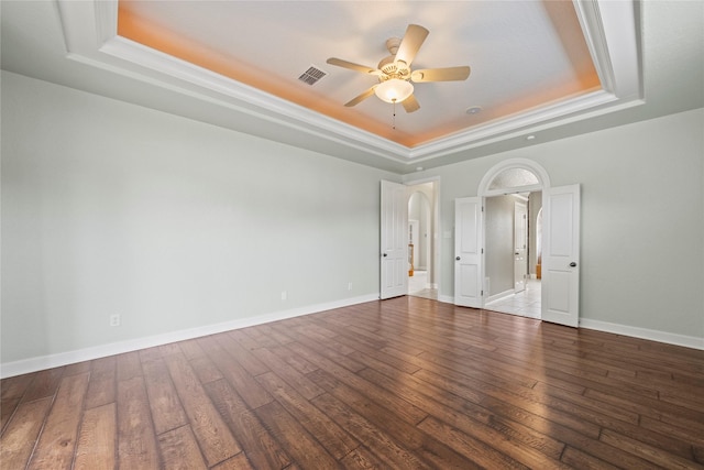 empty room with a tray ceiling, ceiling fan, dark wood-type flooring, and ornamental molding