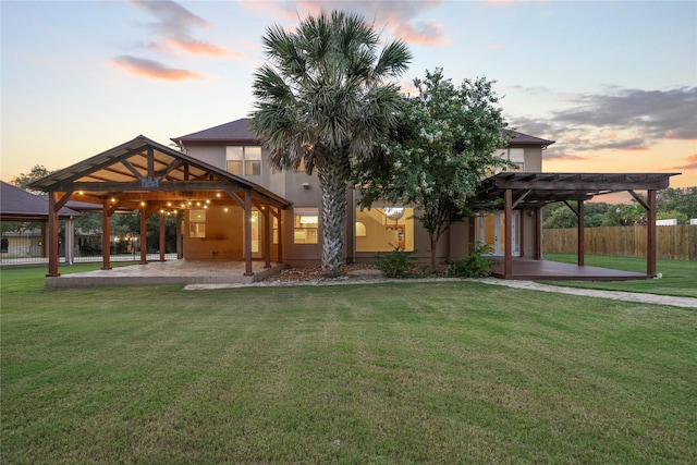 back house at dusk featuring a lawn, a patio area, and a pergola