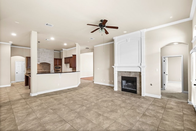 unfurnished living room with ornamental molding, ceiling fan, and a tiled fireplace