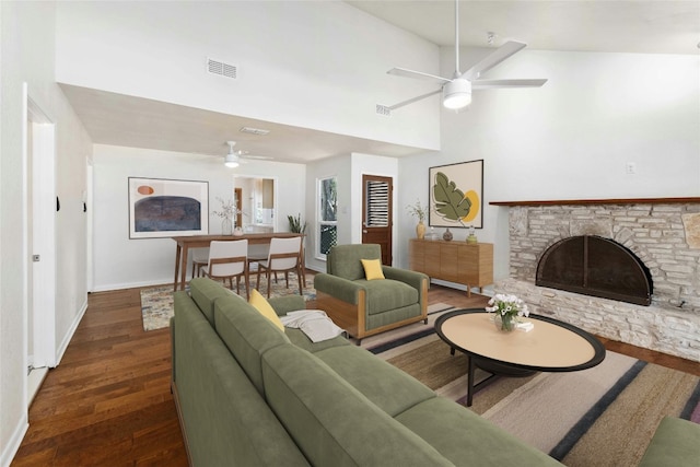 living room with high vaulted ceiling, ceiling fan, dark wood-type flooring, and a stone fireplace