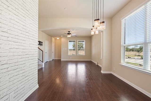 spare room with dark wood-type flooring, brick wall, and ceiling fan with notable chandelier