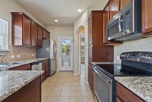 kitchen featuring appliances with stainless steel finishes, light stone counters, backsplash, sink, and light tile floors