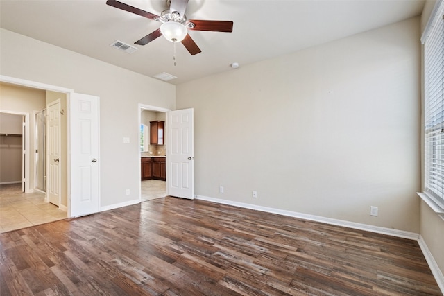 unfurnished bedroom with dark hardwood / wood-style floors, ceiling fan, a closet, ensuite bath, and a walk in closet