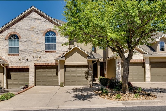 townhome / multi-family property with a garage, concrete driveway, stone siding, and stucco siding