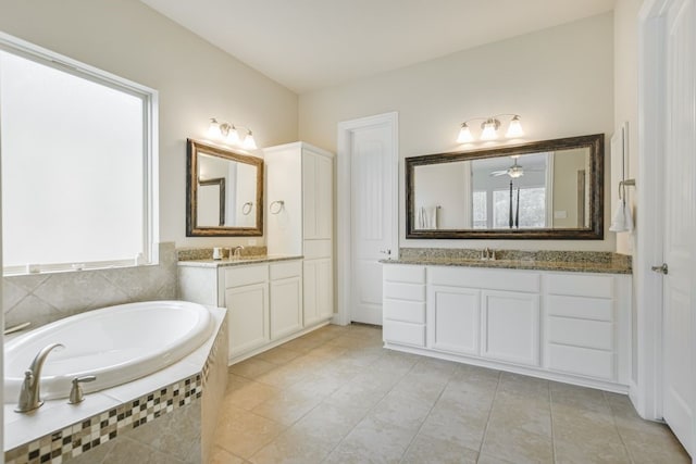 bathroom with dual bowl vanity, tile flooring, tiled tub, and ceiling fan