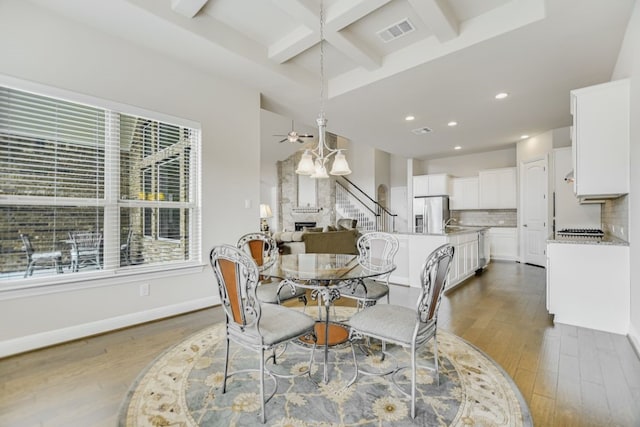 dining space featuring ceiling fan, beam ceiling, a fireplace, wood-type flooring, and coffered ceiling