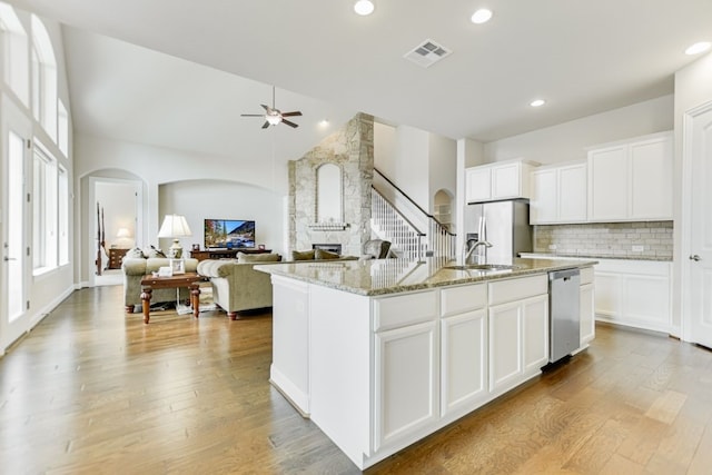 kitchen featuring a stone fireplace, white cabinetry, a kitchen island with sink, and light wood-type flooring