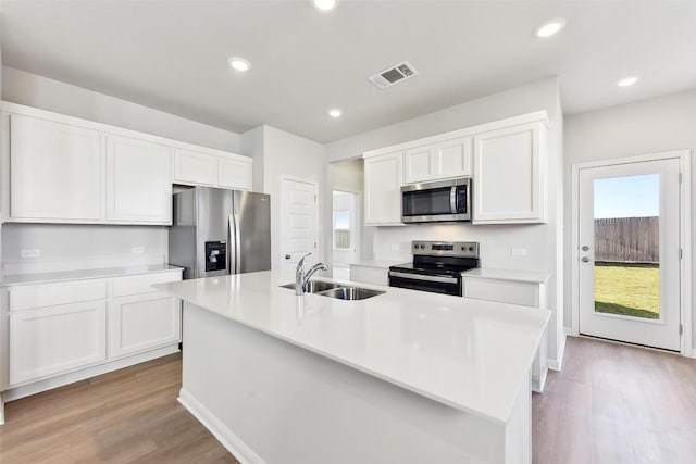 kitchen with an island with sink, appliances with stainless steel finishes, white cabinets, and a sink