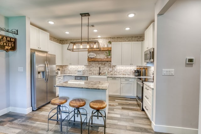 kitchen featuring a breakfast bar, stainless steel appliances, sink, white cabinets, and a center island