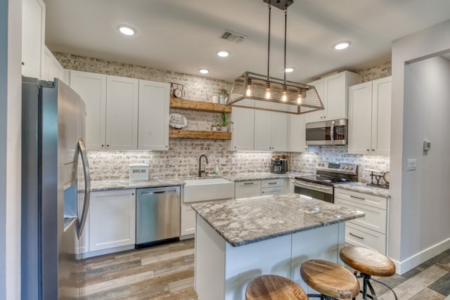 kitchen featuring appliances with stainless steel finishes, a center island, decorative light fixtures, and white cabinetry