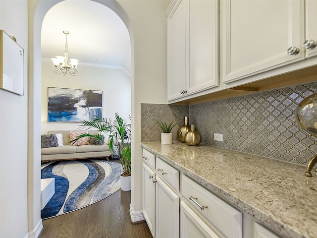 bar with tasteful backsplash, white cabinets, dark wood-type flooring, light stone counters, and ornamental molding