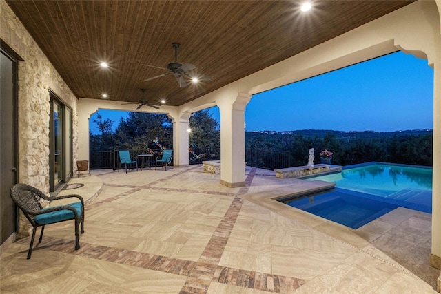 pool at dusk with ceiling fan, a patio area, and an in ground hot tub