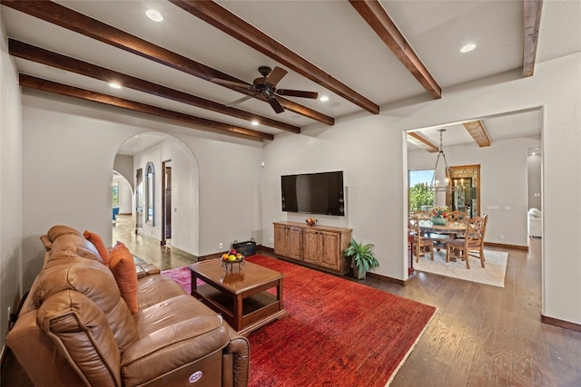 living room featuring dark hardwood / wood-style flooring, beamed ceiling, and ceiling fan with notable chandelier