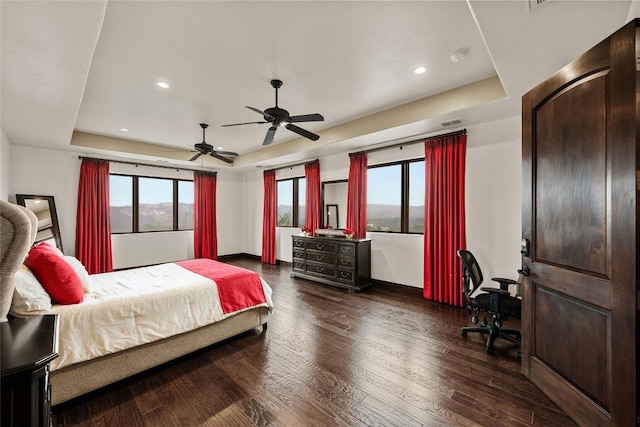 bedroom with ceiling fan, dark wood-type flooring, and a tray ceiling