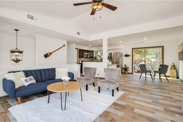 living room featuring ceiling fan with notable chandelier, light wood-type flooring, and lofted ceiling