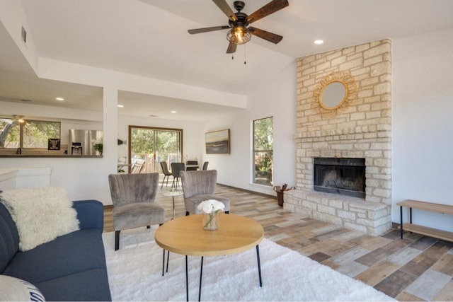 living room with a fireplace, ceiling fan, light hardwood / wood-style flooring, and vaulted ceiling