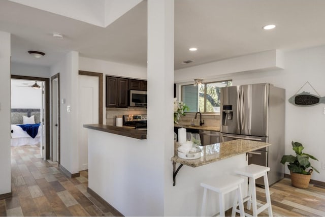 kitchen with a breakfast bar, kitchen peninsula, appliances with stainless steel finishes, tasteful backsplash, and dark brown cabinetry