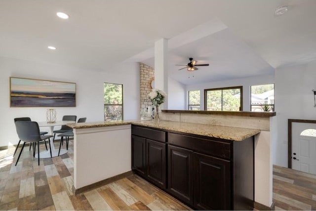 kitchen featuring lofted ceiling, light hardwood / wood-style flooring, ceiling fan, light stone countertops, and kitchen peninsula