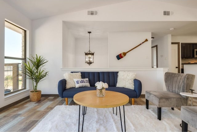 living area with an inviting chandelier, vaulted ceiling, a healthy amount of sunlight, and light hardwood / wood-style flooring