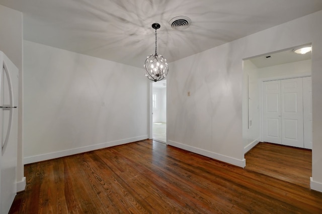 spare room with a notable chandelier and dark hardwood / wood-style flooring