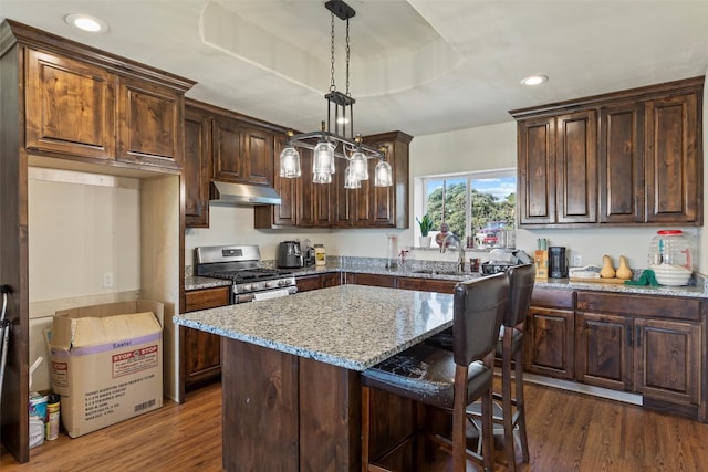 kitchen featuring gas stove, hanging light fixtures, dark hardwood / wood-style flooring, and light stone counters