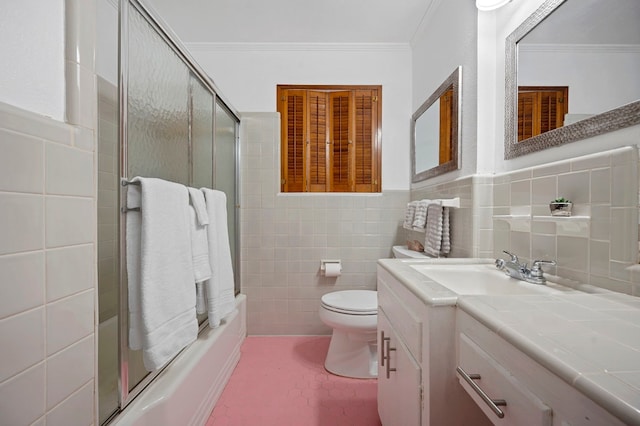 full bathroom featuring bath / shower combo with glass door, tile walls, vanity, toilet, and crown molding