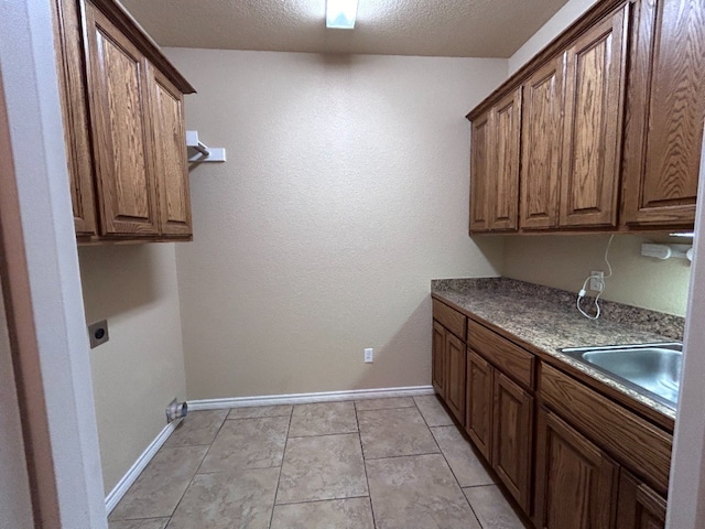 clothes washing area featuring cabinets, a textured ceiling, electric dryer hookup, sink, and light tile patterned floors