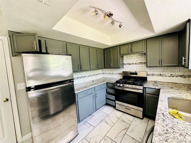 kitchen with backsplash, appliances with stainless steel finishes, a raised ceiling, and rail lighting