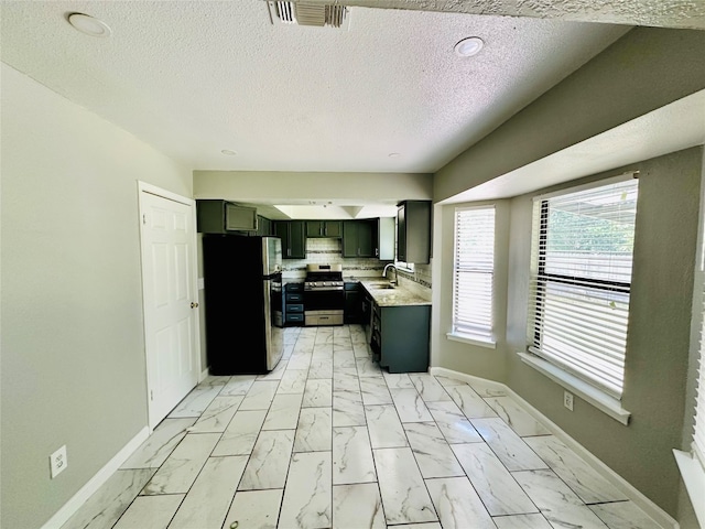 kitchen featuring a textured ceiling, stainless steel range oven, backsplash, refrigerator, and light tile floors