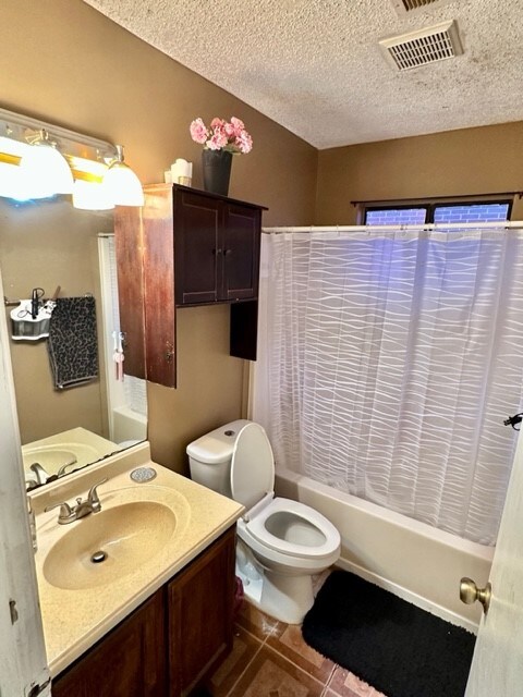 full bathroom featuring toilet, vanity, tile patterned floors, a textured ceiling, and shower / bath combination with curtain