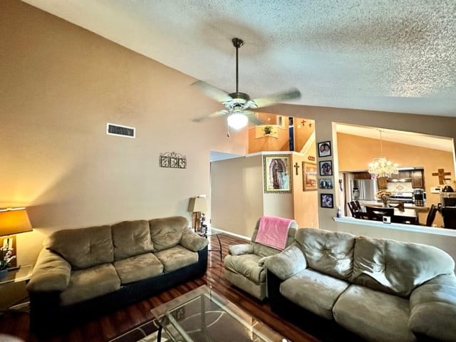 living room featuring ceiling fan with notable chandelier, a textured ceiling, and lofted ceiling