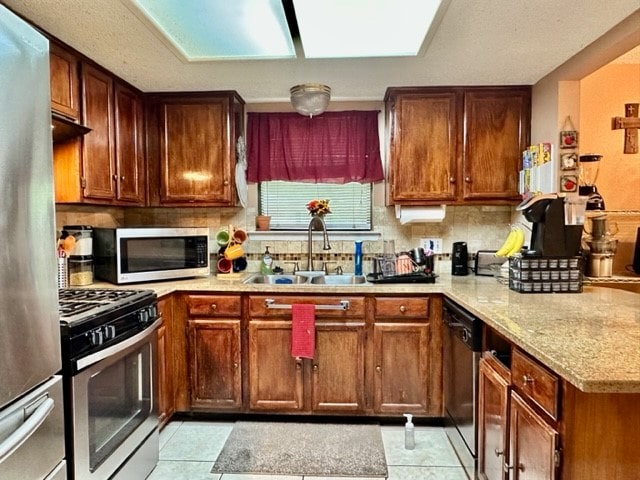 kitchen with sink, appliances with stainless steel finishes, decorative backsplash, light stone countertops, and light tile patterned floors