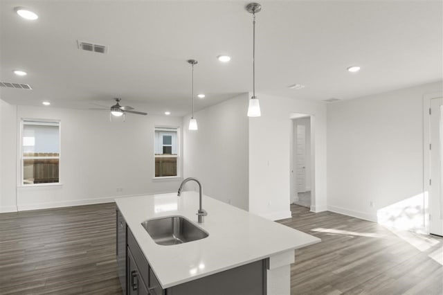 kitchen with dark wood-type flooring, decorative light fixtures, sink, and a kitchen island with sink