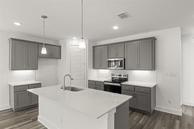 kitchen with an island with sink, stainless steel appliances, dark wood-type flooring, sink, and gray cabinets