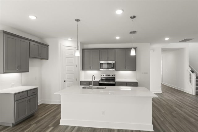 kitchen featuring appliances with stainless steel finishes, gray cabinetry, a kitchen island with sink, and decorative light fixtures