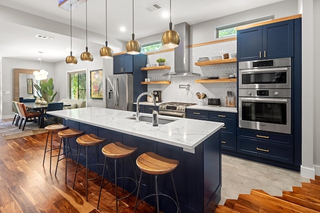 kitchen with light hardwood / wood-style floors, a kitchen island with sink, blue cabinets, island exhaust hood, and stainless steel appliances