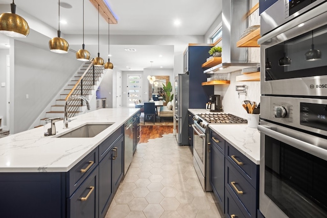 kitchen featuring wall chimney exhaust hood, blue cabinets, pendant lighting, sink, and appliances with stainless steel finishes