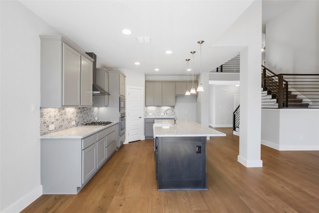 kitchen featuring hanging light fixtures, gray cabinetry, an island with sink, hardwood / wood-style floors, and stainless steel oven